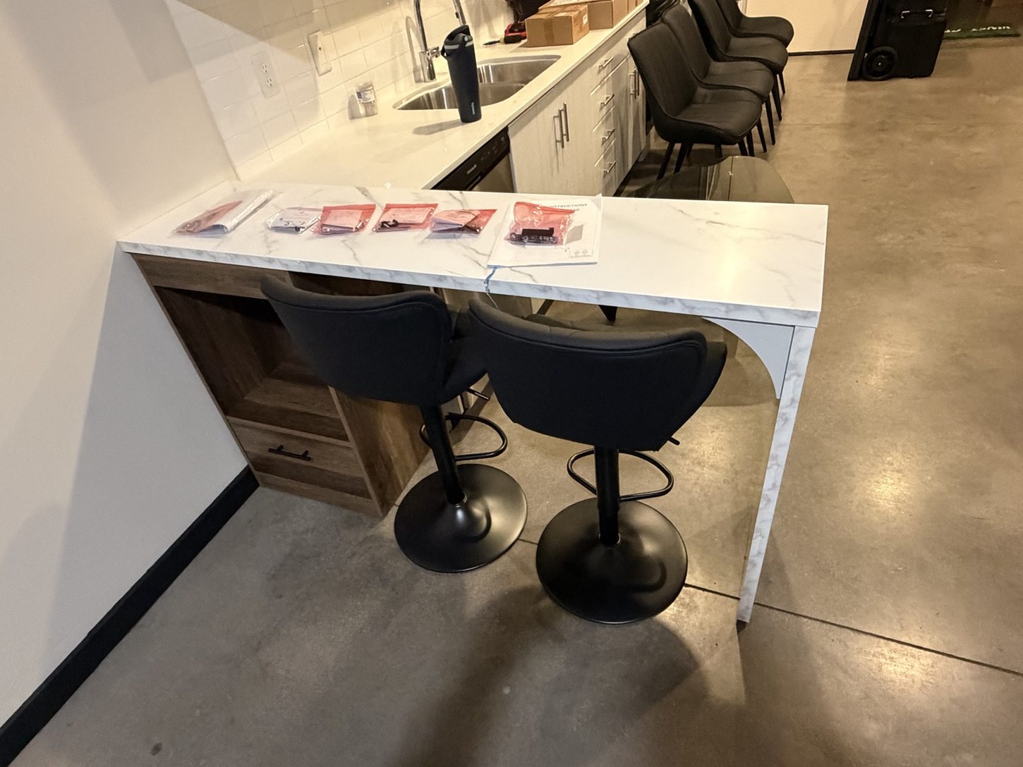 Marble-look cabinet and breakfast bar with two black stools and organized spare hardware